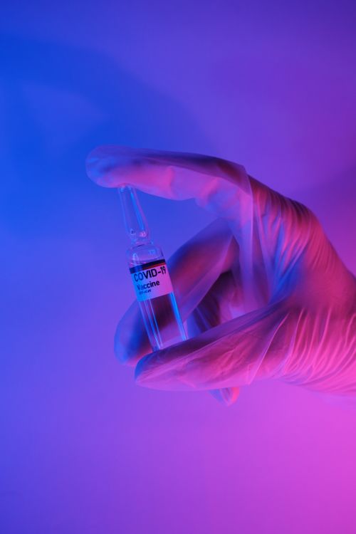 Free Crop faceless scientist in latex medical gloves demonstrating ampoule with COVID 19 vaccine in modern laboratory in bright neon illumination Stock Photo