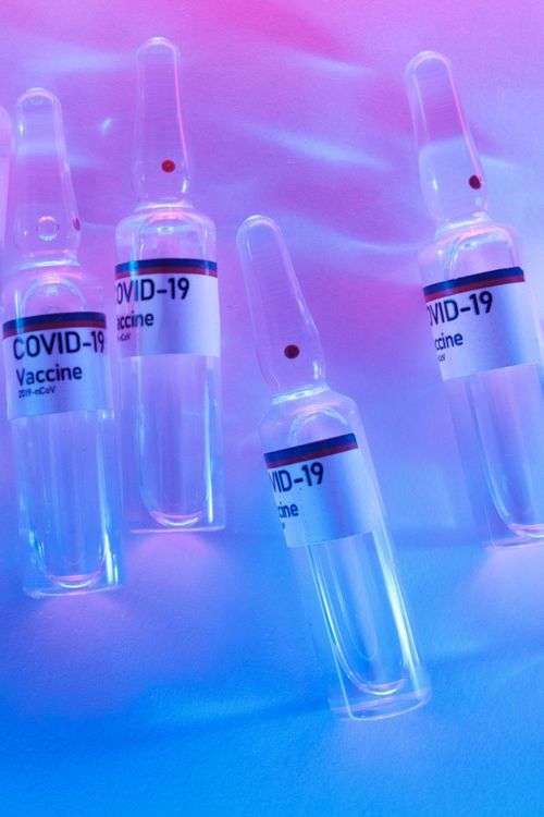 Free Set of sealed ampoules with transparent liquid vaccine against coronavirus placed on tables in laboratory with colorful illumination Stock Photo