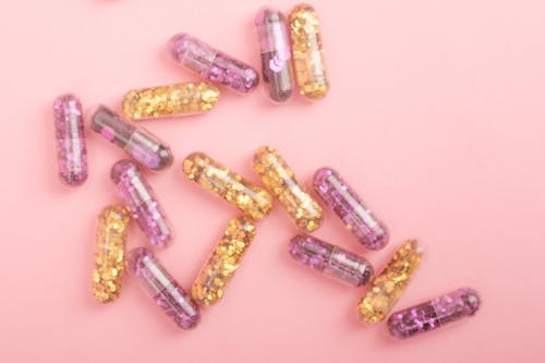 Free Pile of sparkling drug capsules scattered on pink surface Stock Photo