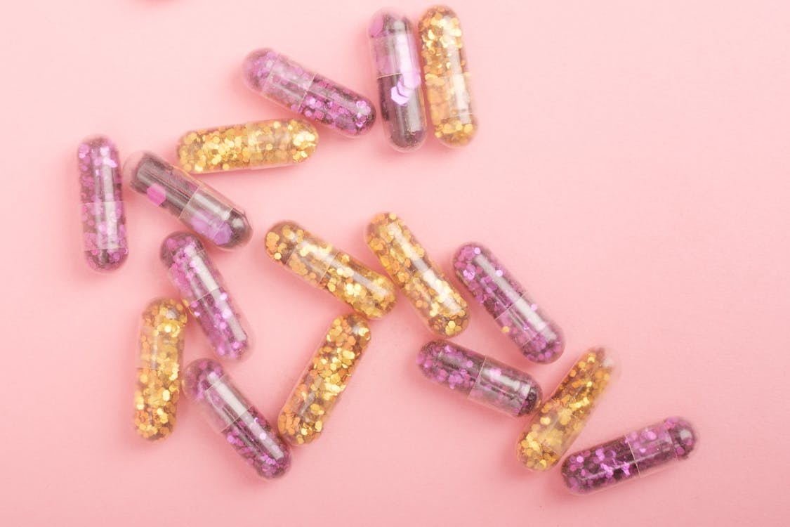 Pile of sparkling drug capsules scattered on pink surface