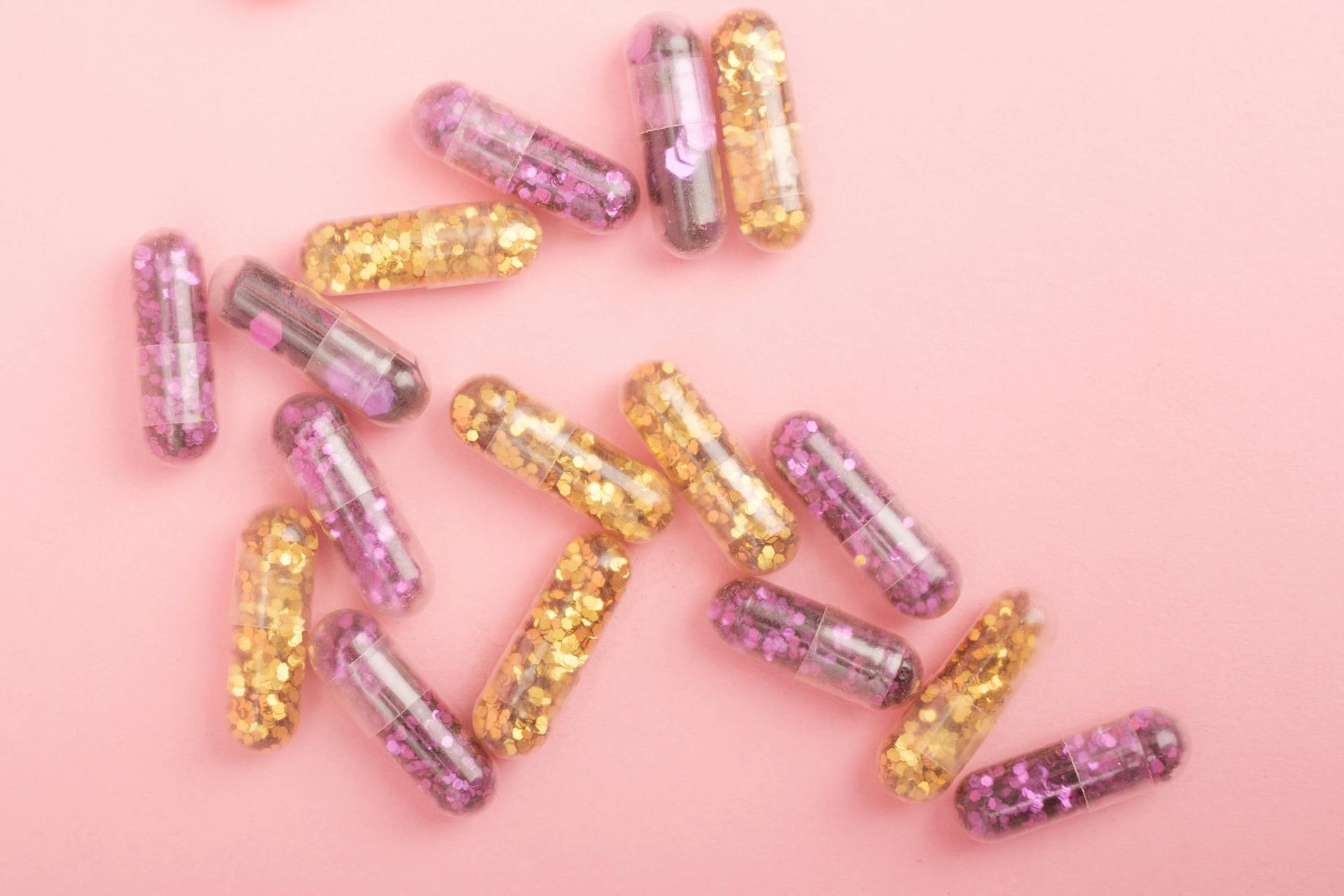 Pile of sparkling drug capsules scattered on pink surface