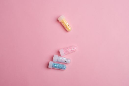 Top view of glass tubes filled with colorful sparkling star shaped glitter scattered on pink table