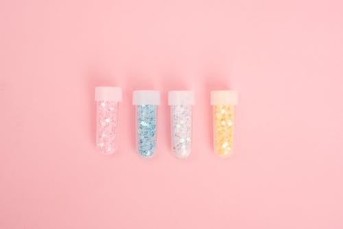 Laboratory tubes with colorful glitter on pink desk