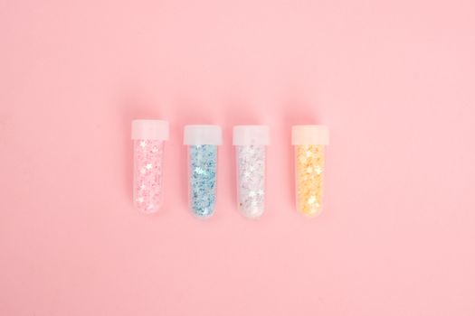 Laboratory tubes with colorful glitter on pink desk