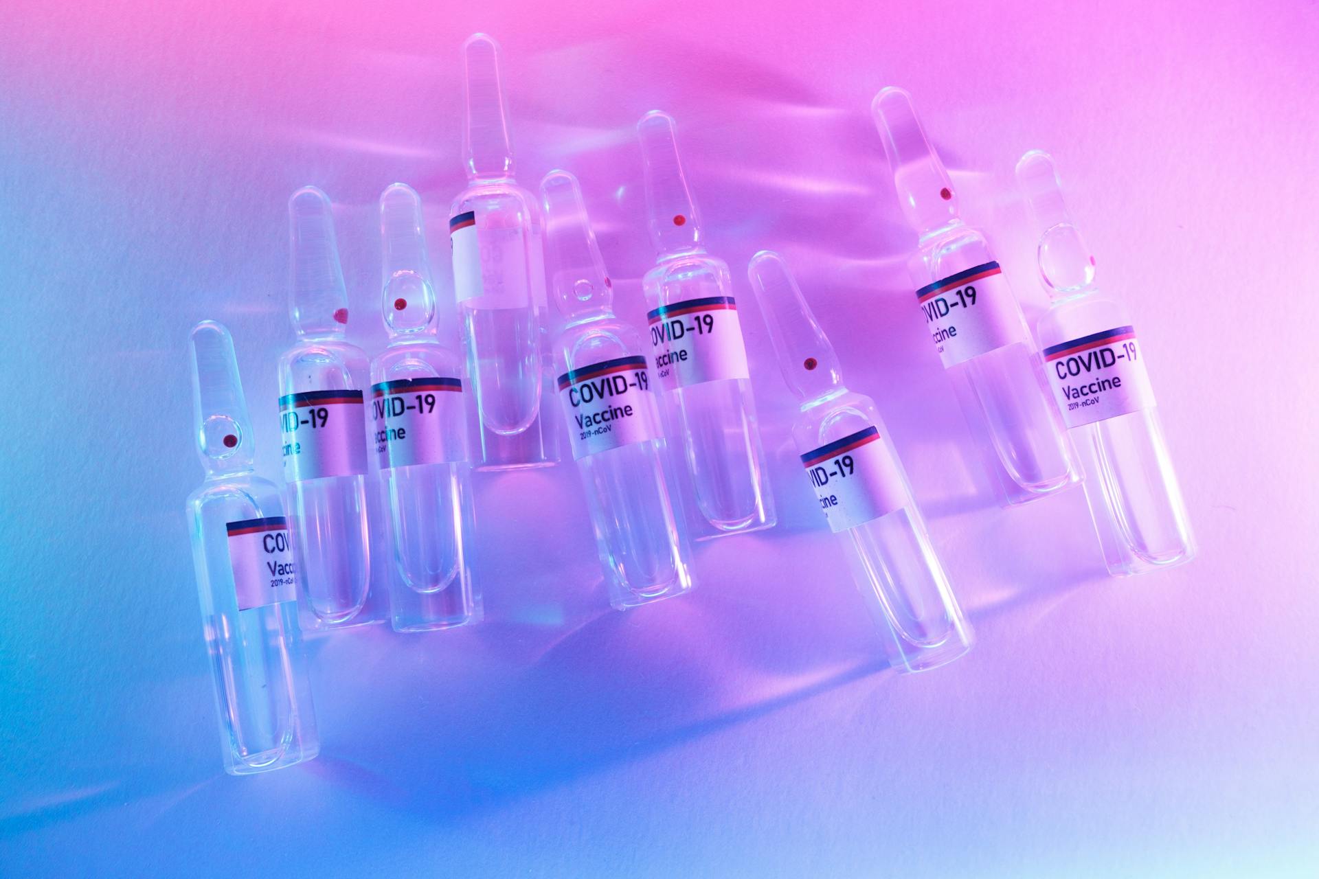 From above pile of doses of COVID 19 vaccine in similar ampoules placed on desk in laboratory with neon lights