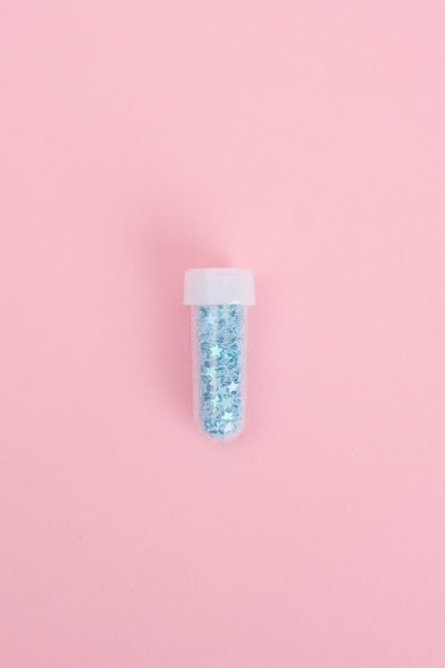 Top view of bright blinking glitter packed into glass tube on pink background