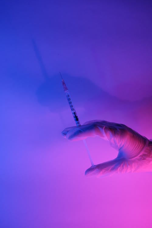 Free Syringe with useful medical vaccine for coronavirus in neon purple and blue light Stock Photo