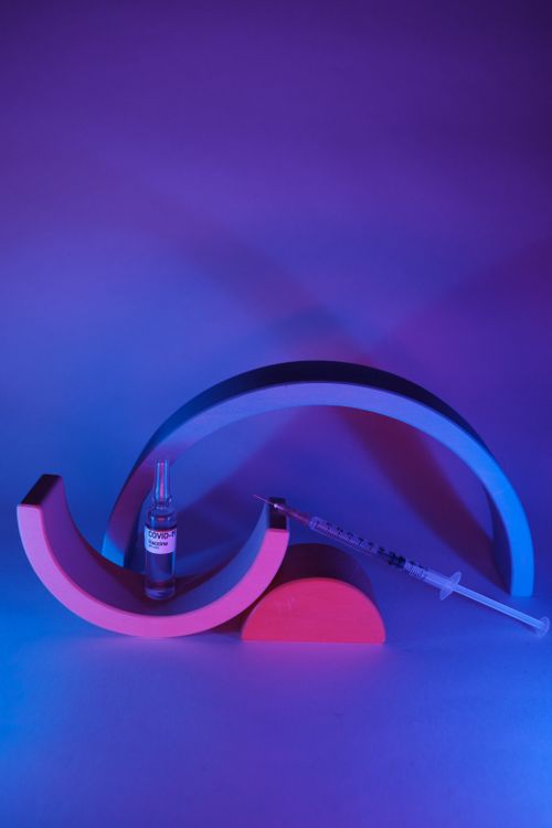 Free Glass ampoule with useful vaccine for coronavirus and syringe prepared for medical injection in neon light Stock Photo