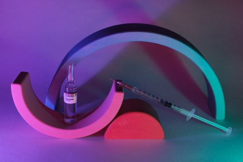 Free Vaccine for coronavirus in glass ampoule and syringe with needle in neon light Stock Photo