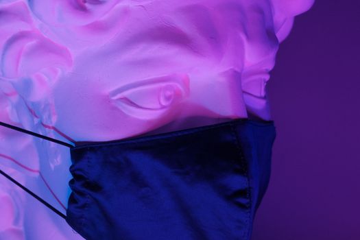 White sculpture of Apollo with medical mask on face in bright neon light on purple background