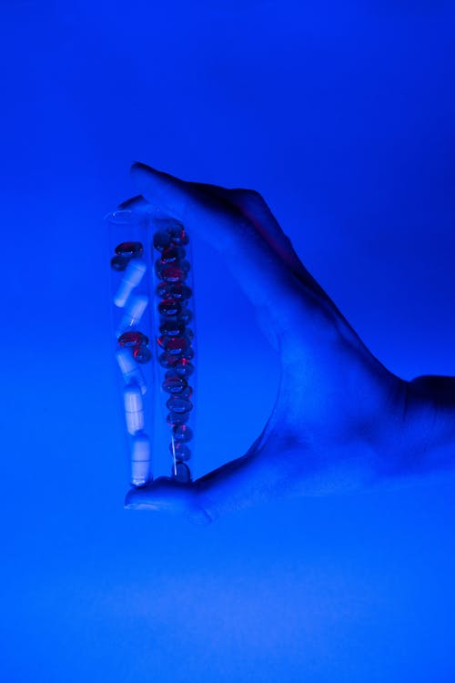 Vials with pills and capsules in ultraviolet light in hand