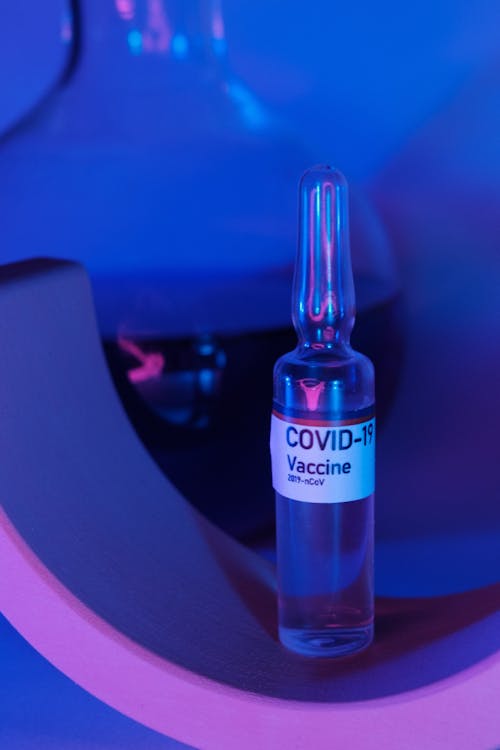 Glass ampoule with vaccine for COVID 19 near flask with fluid in ultraviolet light