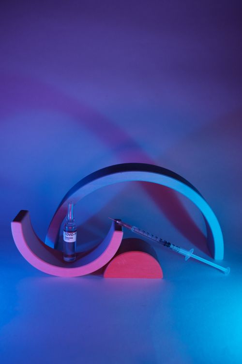 Free Syringe near ampoule with vaccine for coronavirus with geometric decor in ultraviolet light Stock Photo
