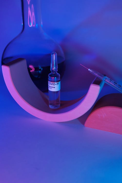 Vaccine for coronavirus on geometrical decor near syringe with needle and glass flask with liquid