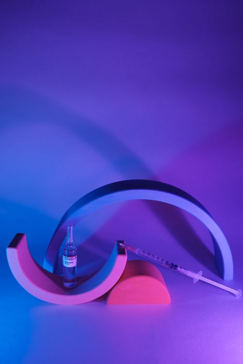Free Ampoule with vaccine for coronavirus for injection on geometrical figures in ultraviolet light Stock Photo