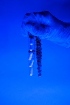 Tubes with different capsules and pills in hand in medical glove in ultraviolet light