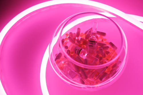 From above of glassware with capsules and ampoules with vaccine for coronavirus in neon light