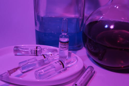 Ampoules with vaccine for COVID 19 near glass flasks