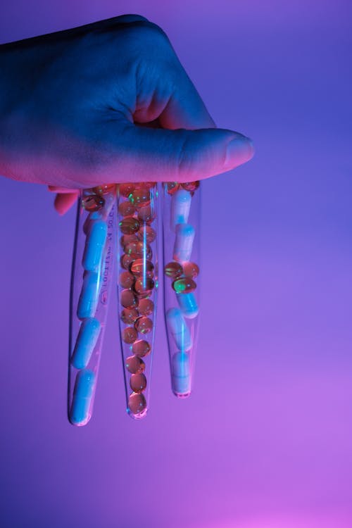 Transparent fragile glass tubes full of different capsules and pills in ultraviolet light