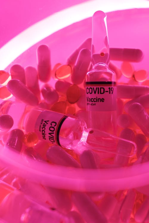 Ampoules with vaccine for coronavirus among capsules in bowl in bright neon light