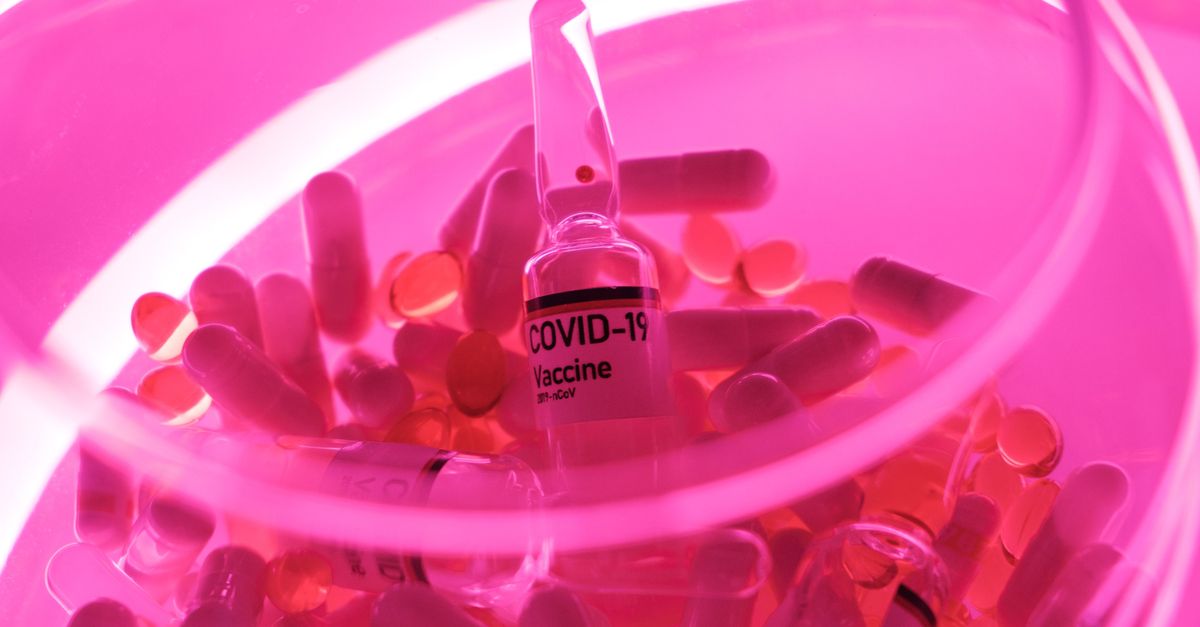 From above of glass fragile bowl with vaccine for COVID 19 and capsules in neon light