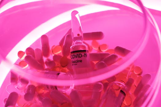 An artistic shot of a COVID-19 vaccine vial surrounded by capsules under vibrant neon lighting.