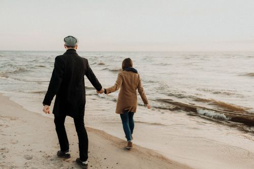 Free Couple holding hands while walking along a serene beach shoreline, enjoying the ocean view. Stock Photo
