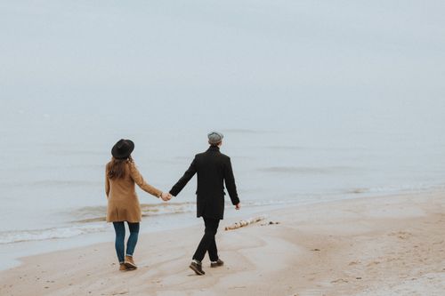 Free A couple holding hands and walking along a serene beach on a misty day. Stock Photo