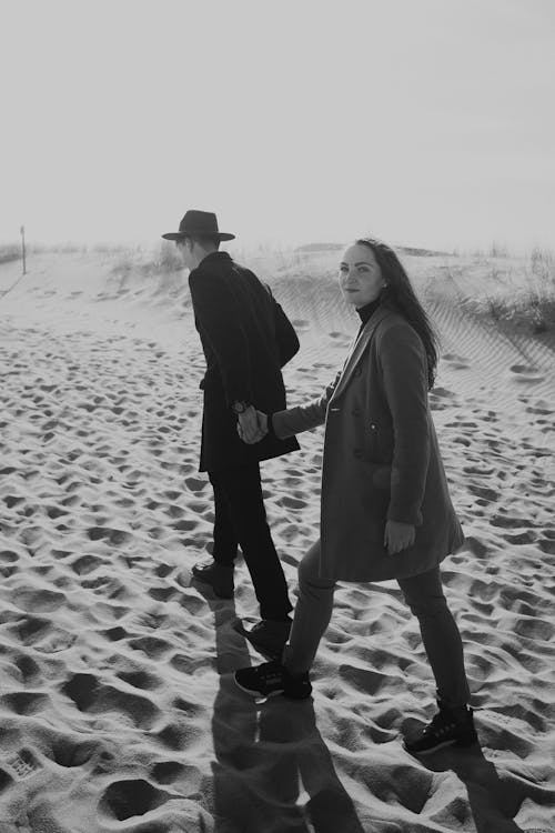 A Grayscale Photo of a Couple Walking on Sand