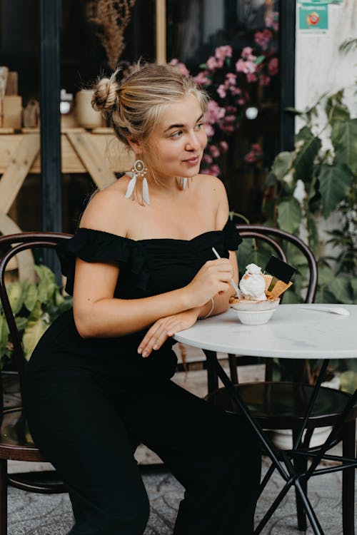 A Woman Wearing a Black Off-Shoulder Outfit Eating Ice Cream