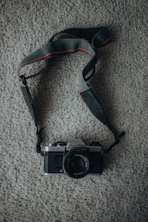 Free Top view of old fashioned black photo camera with lens and dark strap placed on rug with shadow in room Stock Photo
