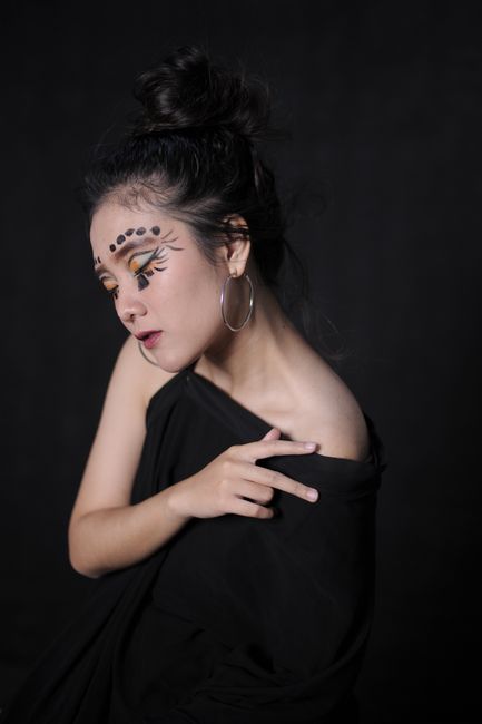 Striking portrait of a woman with creative face paint posing against a dark background.