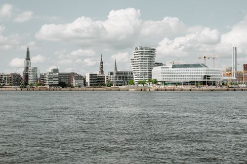 Free Cityscape with contemporary multistory buildings and skyscrapers placed on shore of river with rippled water under cloudy sky Stock Photo
