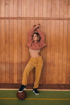 Stylish woman in a crop top poses indoors against a wooden wall holding a basketball.