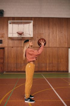 Side view of a woman holding a basketball inside a wooden-paneled court, preparing to shoot.