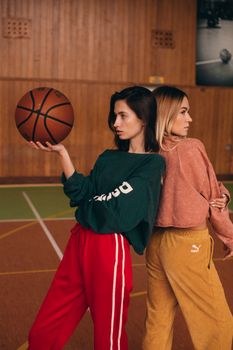 Two women posing with a basketball on an indoor court in vibrant sportswear.