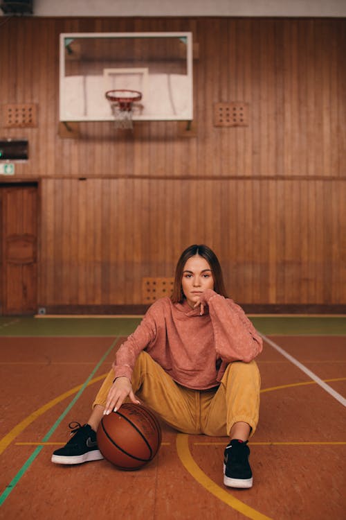 A Woman in Red Long Sleeve Shirt and Brown Pants Sitting on Basketball Court