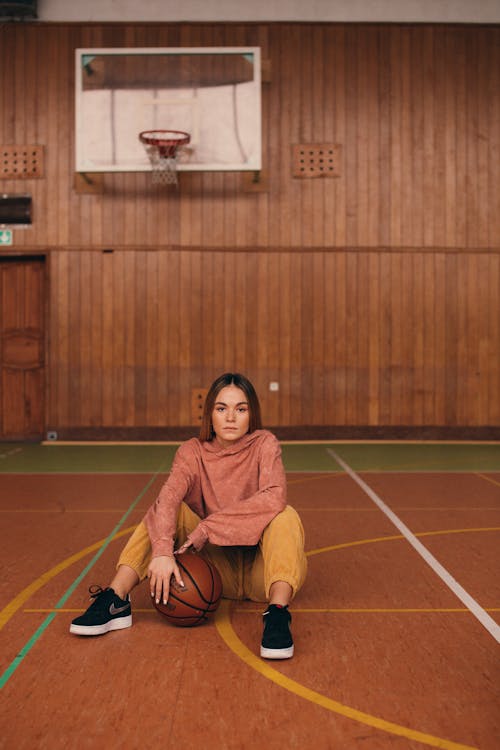 A Woman Sitting on the Floor while Holding a Basketball