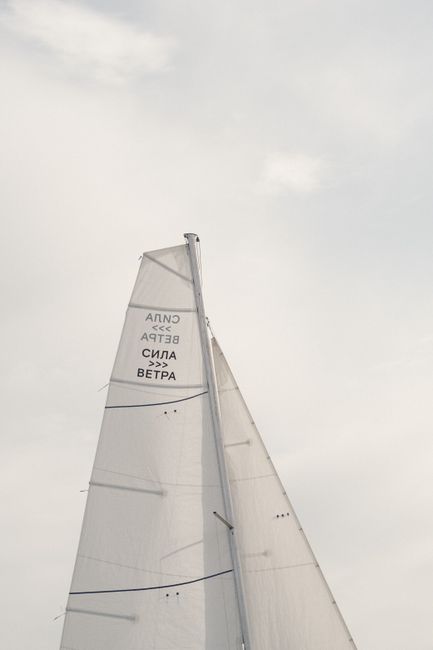 Low angle inscription on tall white sail of boat floating against cloudy sky