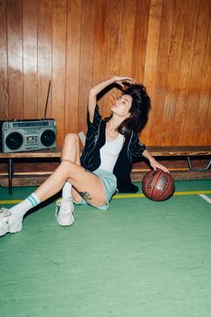 Fashionable woman in casual pose holding a basketball indoors with a retro vibe.