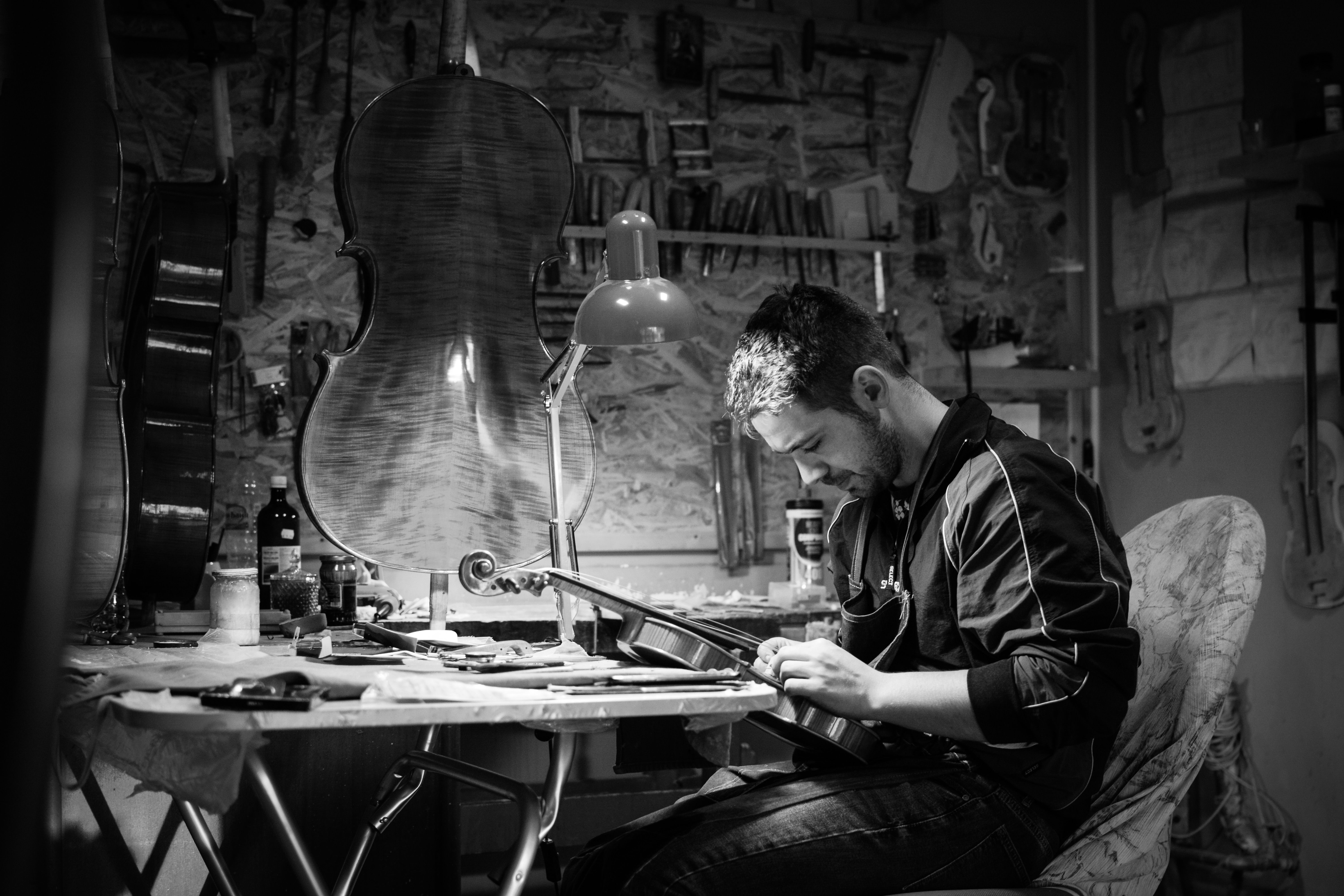Monochrome image of a craftsman working on a violin in a workshop, emphasizing craftsmanship.