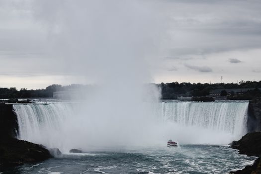 Dramatic view of Niagara Falls with a tour boat below the powerful waterfall.