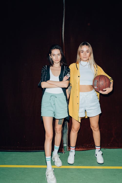 Two Young Women in Shorts Posing with a Basketball