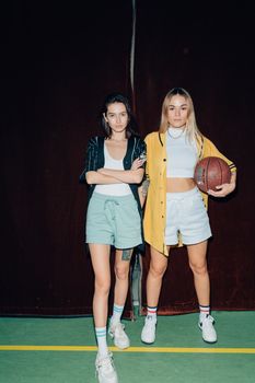 Two stylish women in sporty attire posing confidently with a basketball indoors.