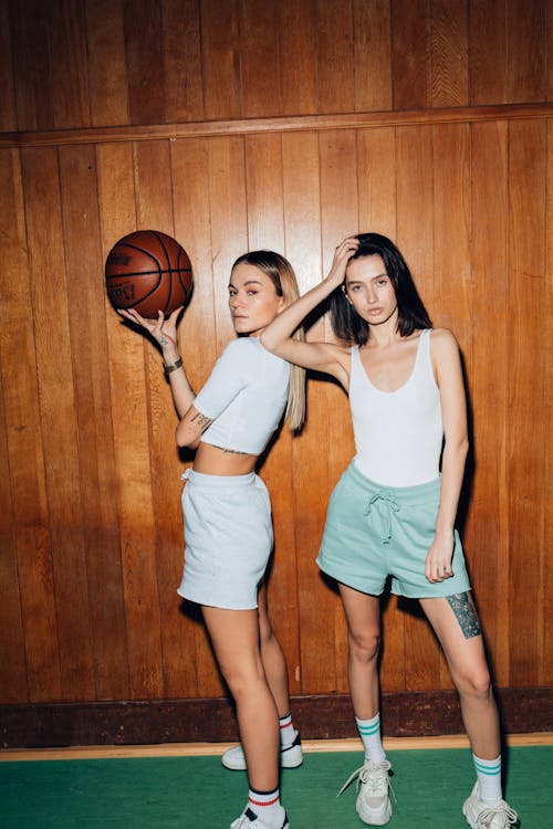 Pretty Young Women in White Tops Posing on Basketball Court