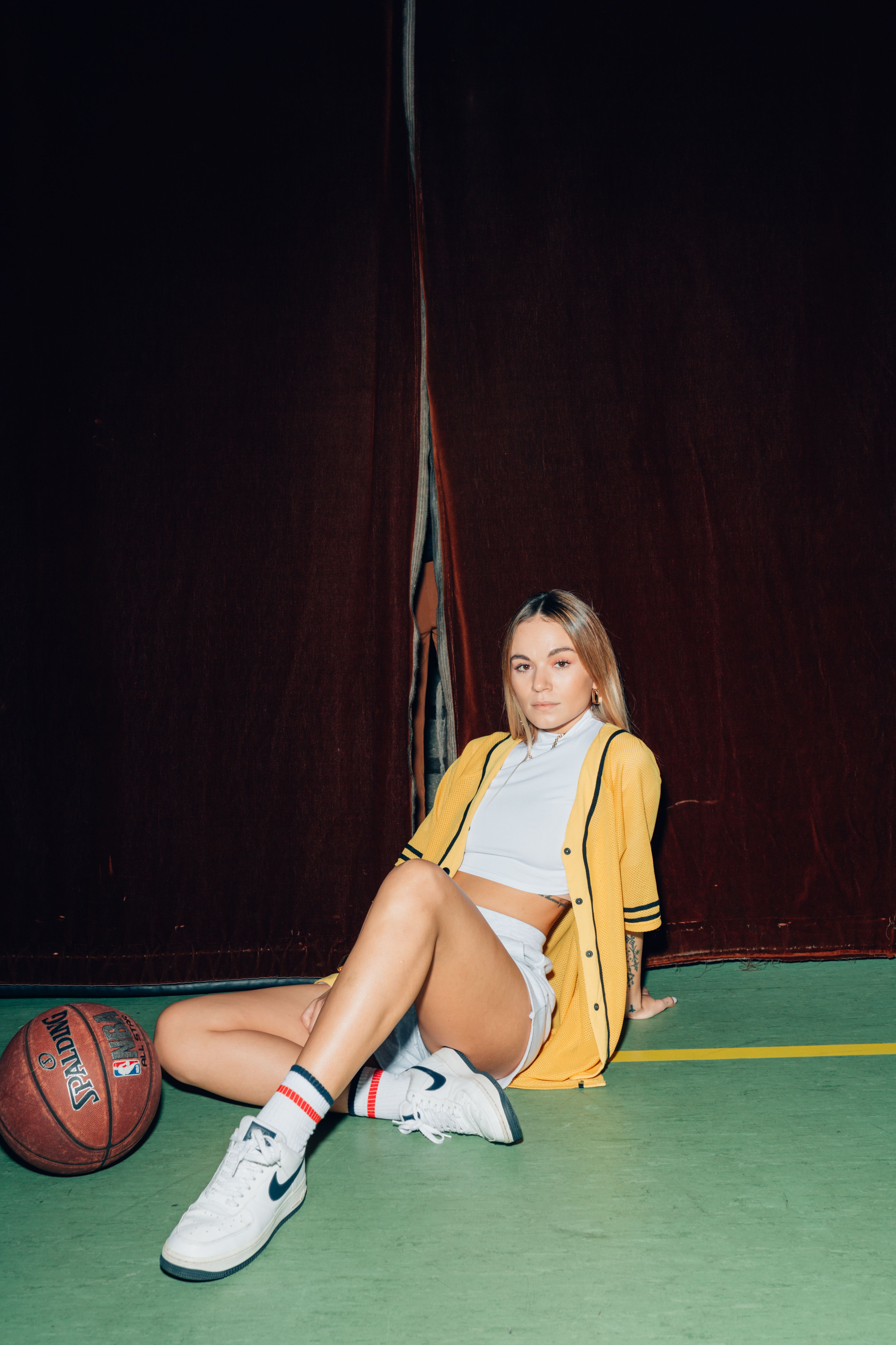 Stylish young woman in yellow jacket posing with basketball in an indoor court.