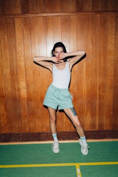 Fashionable woman in green shorts striking a pose indoors against a wooden wall.