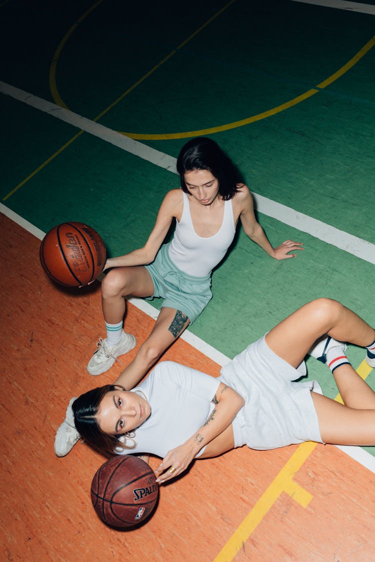 Women Holding Balls Laying On The Basketball Court