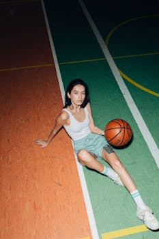 Young woman sitting on a colorful indoor basketball court holding a ball.