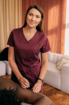Female therapist in burgundy scrub suit provides care in a cozy indoor setting.